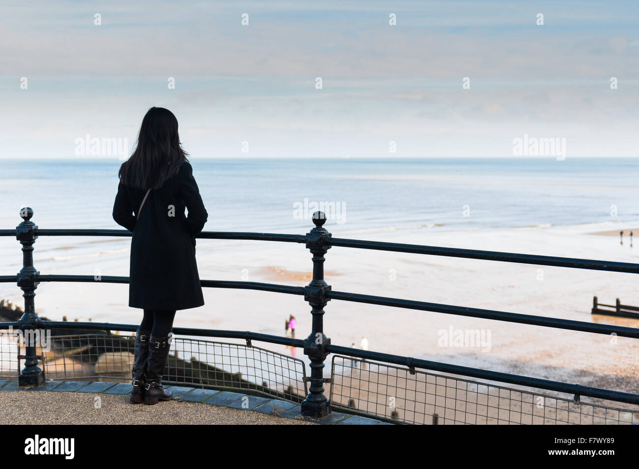 Una giovane donna si affaccia sulla spiaggia e sul mare dal percorso accanto a Cromer Pier Norfolk, Inghilterra, Regno Unito Foto Stock
