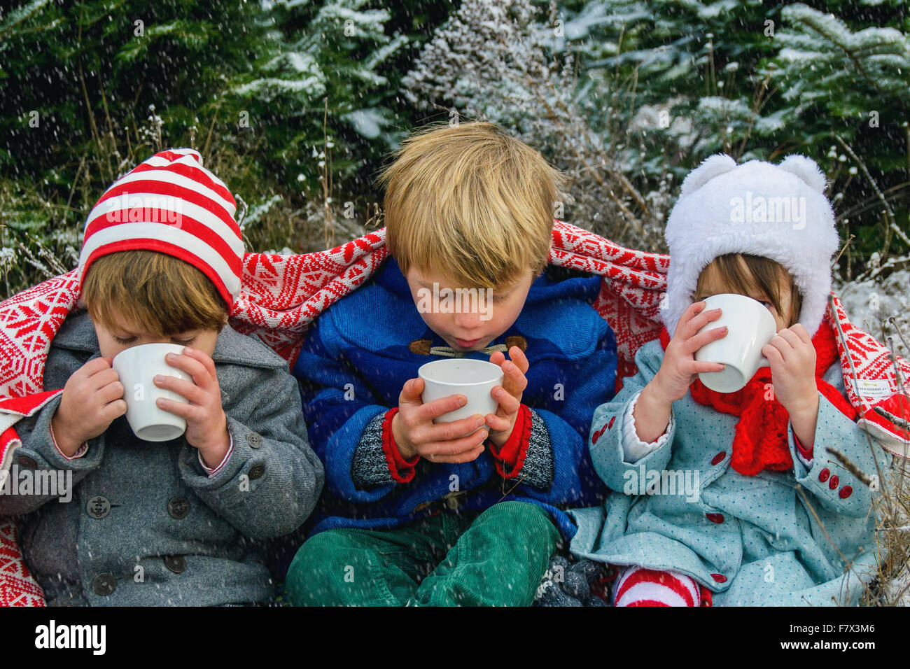Tre bambini avvolti in un mantello seduta nella neve bere cioccolata calda Foto Stock