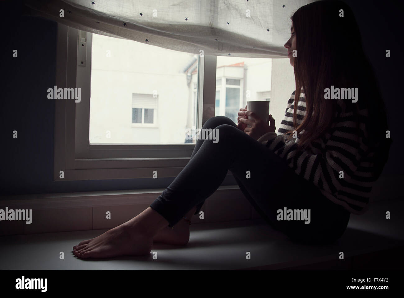 Ragazza seduta da una finestra con una tazza di caffè Foto Stock