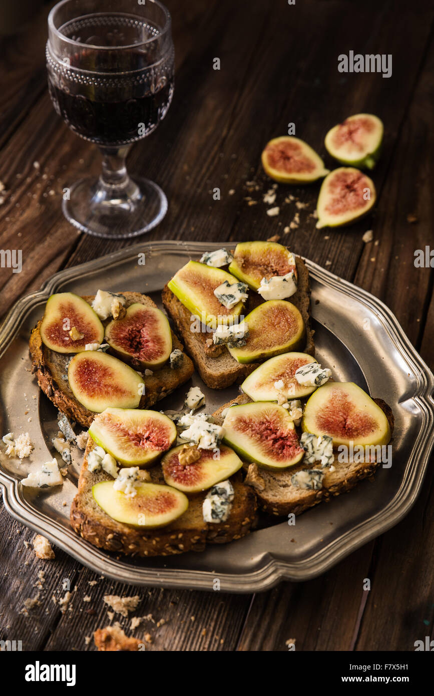 Figg, blu di formaggio e miele su pane tostato con un bicchiere di vino rosso Foto Stock