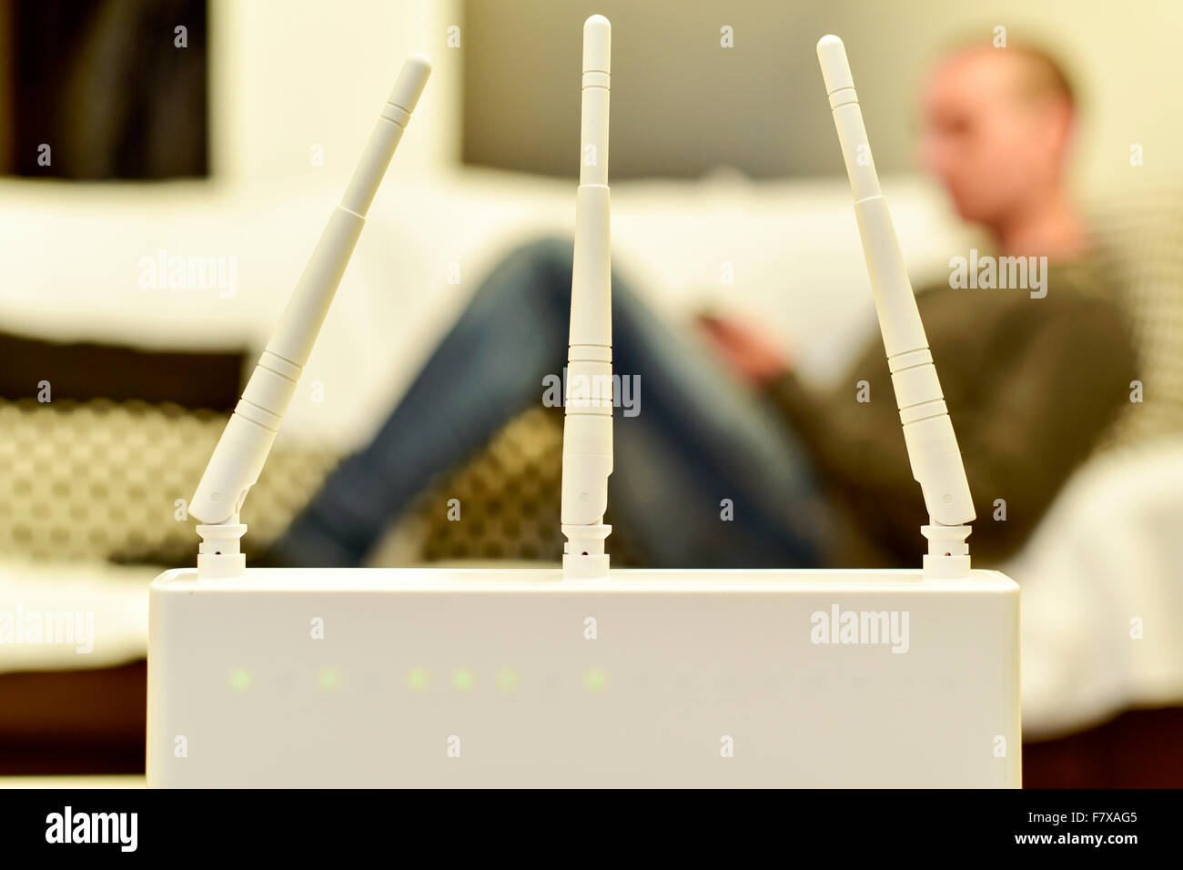 Primo piano di un router wireless e un giovane uomo caucasico utilizzando uno smartphone sdraiato su un lettino in background Foto Stock