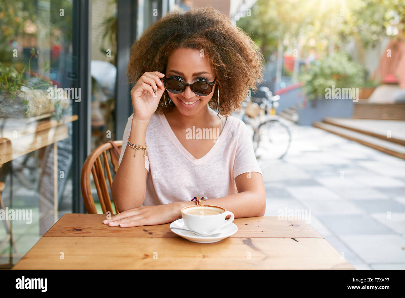 Ritratto di ragazza giovane e carina a outdoor cafe. Giovane donna africana indossando occhiali da sole guardando la fotocamera. Foto Stock