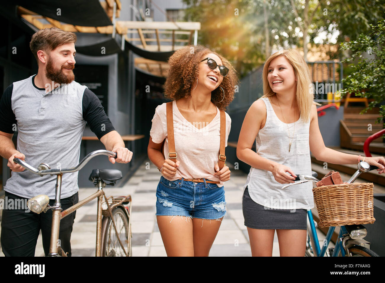 Felici i giovani a piedi giù per la strada di città con le loro biciclette e sorridente. Giovani uomini e donne su strada con le loro biciclette. Foto Stock