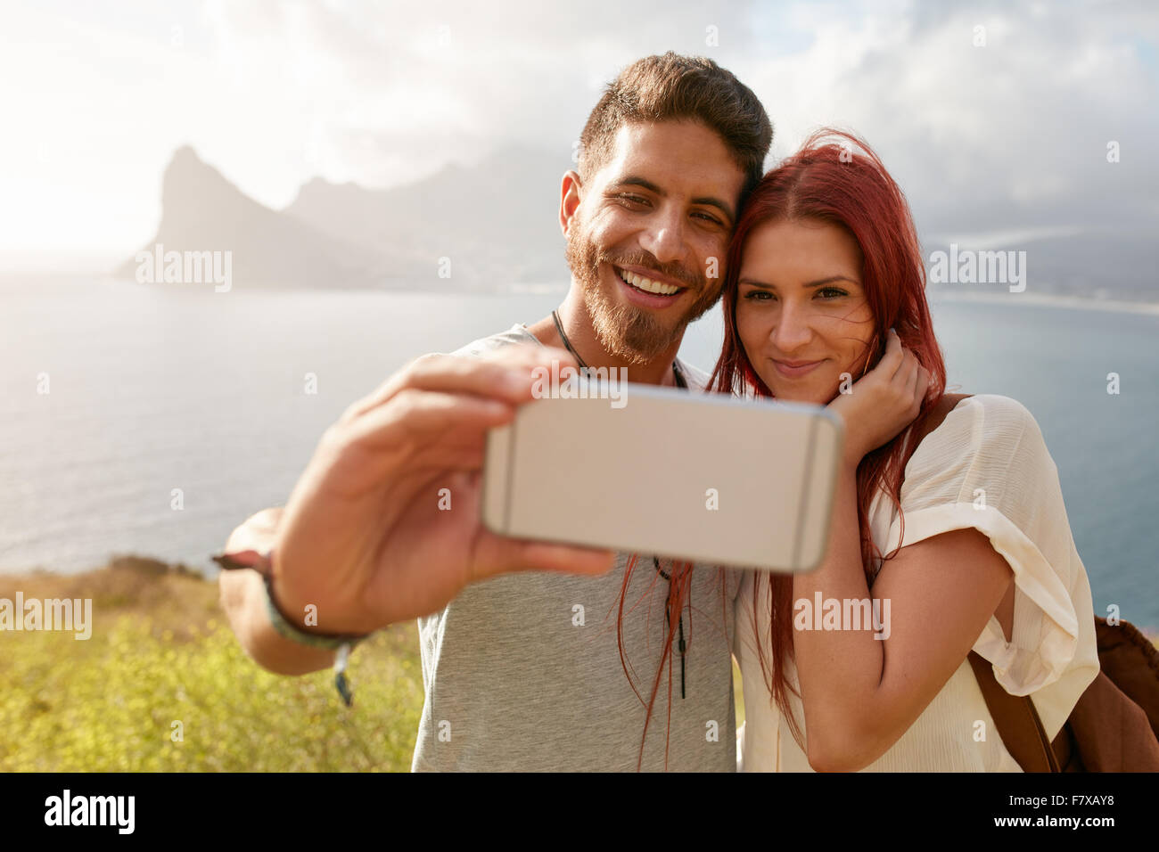 Coppia giovane tenendo autoritratto con la montagna e lo scenario della baia in background. Giovani caucasici uomo prendendo selfie con la sua smart Foto Stock