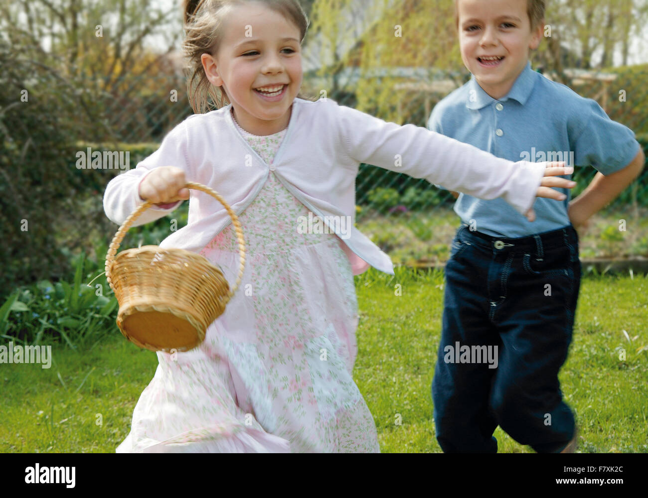 Maedchen mit Osterkoerbchen und Junge rennen im Garten Foto Stock