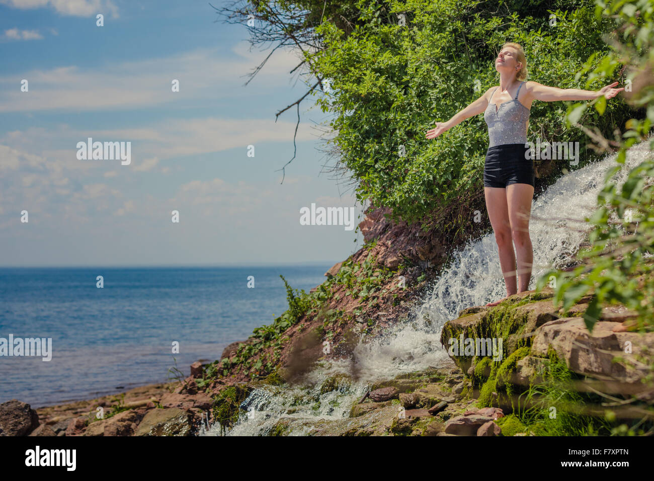 Giovane donna fare yoga posizione di fronte al mare nei pressi di una cascata Foto Stock