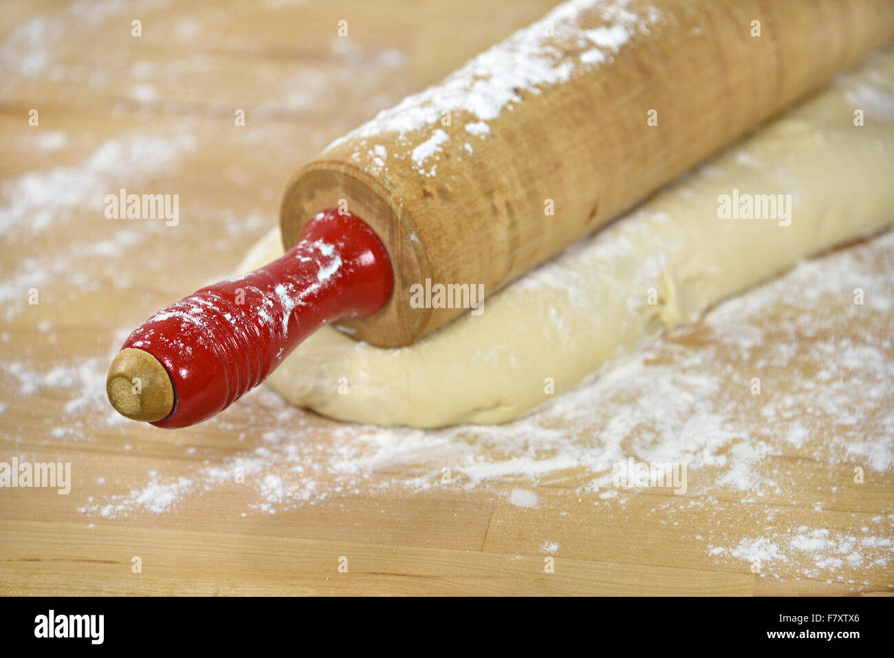 Close up retrò laminazione di legno il perno con la maniglia rossa sulla pasta di pane e farina. Foto Stock