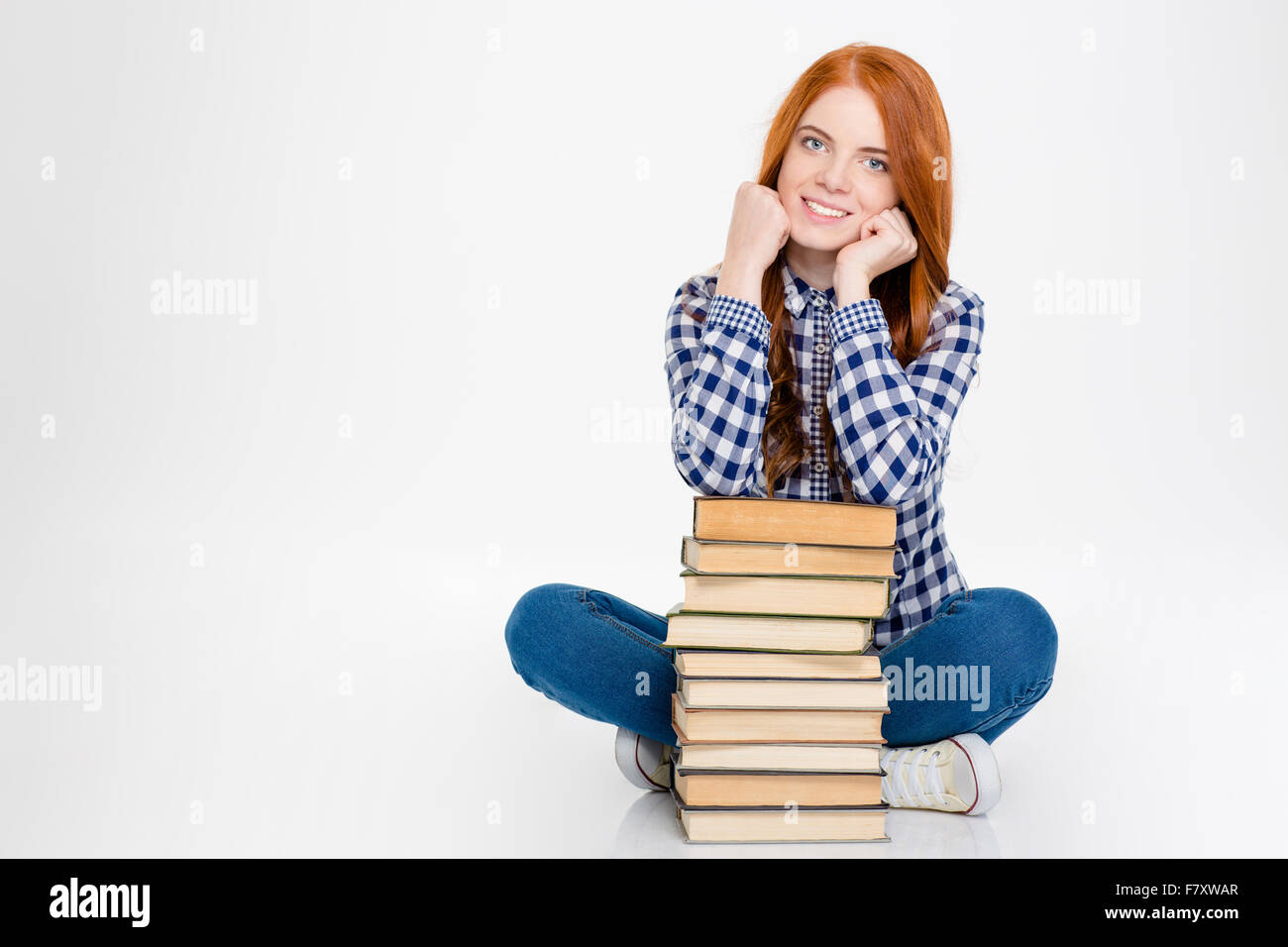 Bella felice redhead giovane ragazza seduta e posa con libri isolate su sfondo bianco Foto Stock