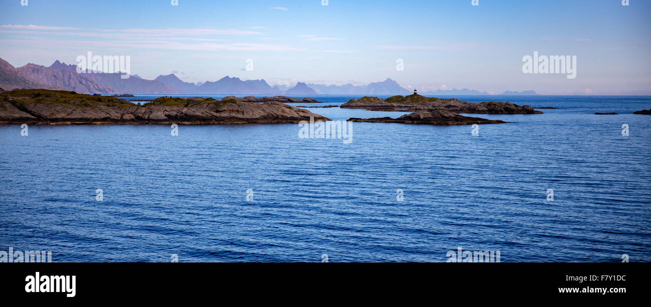 Rocce all'ingresso a Reine harbour con le montagne della parte orientale delle Isole Lofoten in Norvegia a distanza Foto Stock