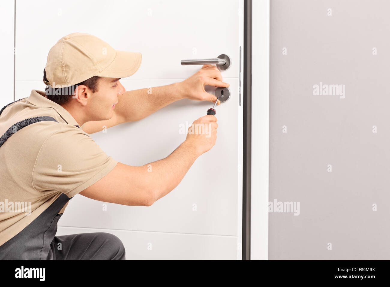 Giovane maschio fabbro installazione di una serratura di una porta di nuovo con un cacciavite Foto Stock