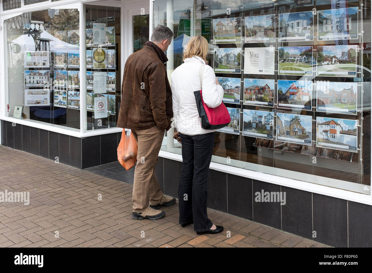 Una coppia di mezza età guardando i dettagli di proprietà attraverso la finestra dell'agente immobiliare, Epsom, Surrey Foto Stock