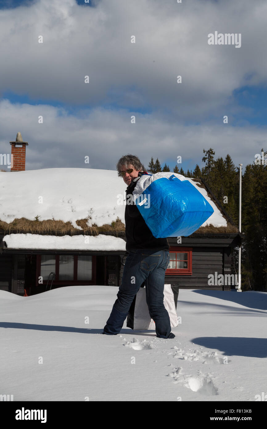 Uomo borse e zaini nella neve profonda di una tradizionale baita norvegese - Ritratto Foto Stock