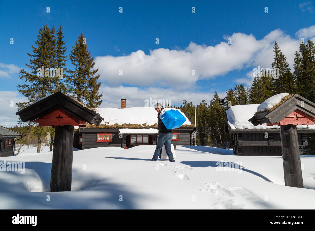 Uomo borse e zaini nella neve profonda di una tradizionale baita norvegese Foto Stock