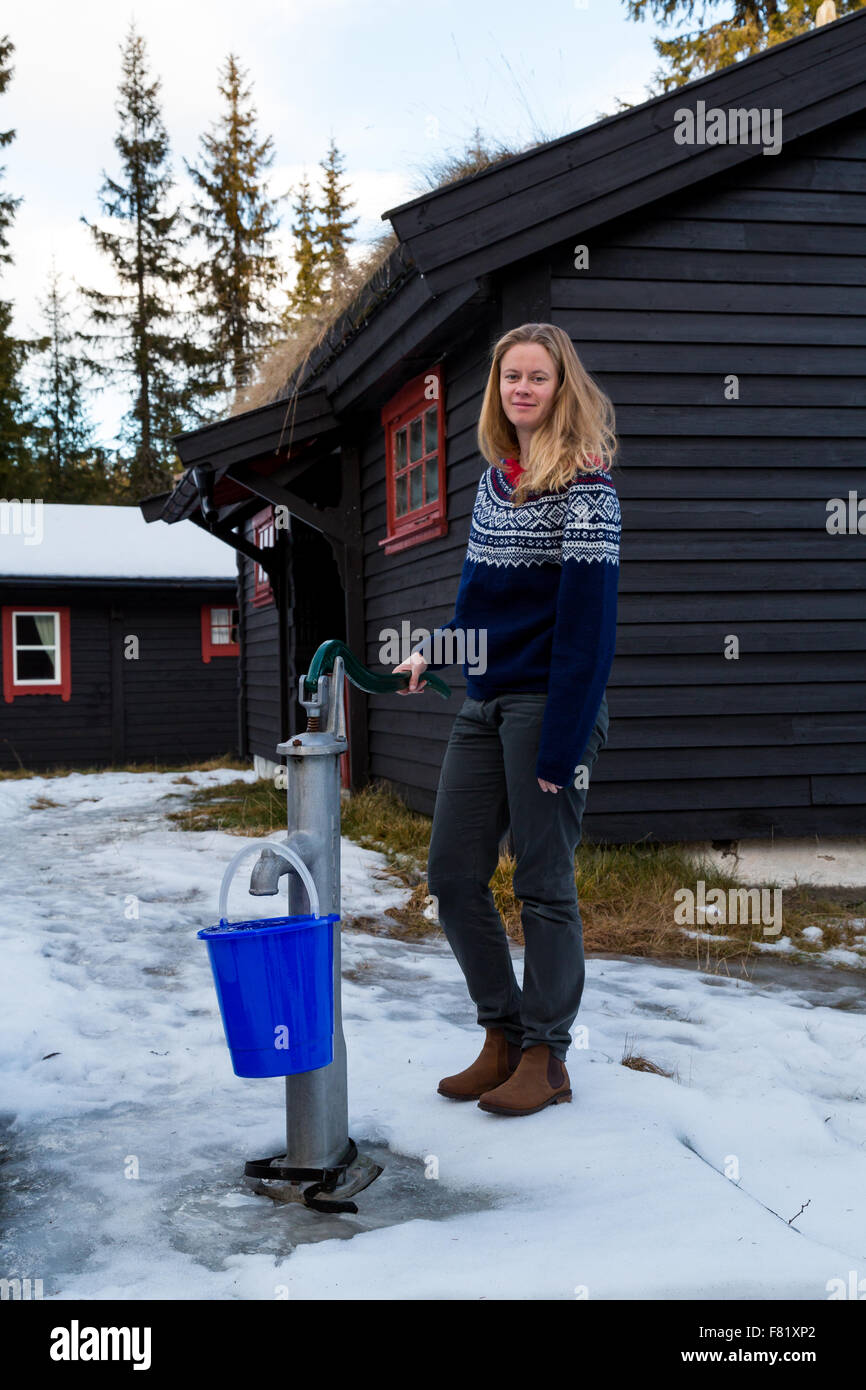 Pretty girl il riempimento di una benna utilizzando una pompa a mano da un pozzo al di fuori di una cabina nella foresta a nord di Oslo - Ritratto Foto Stock