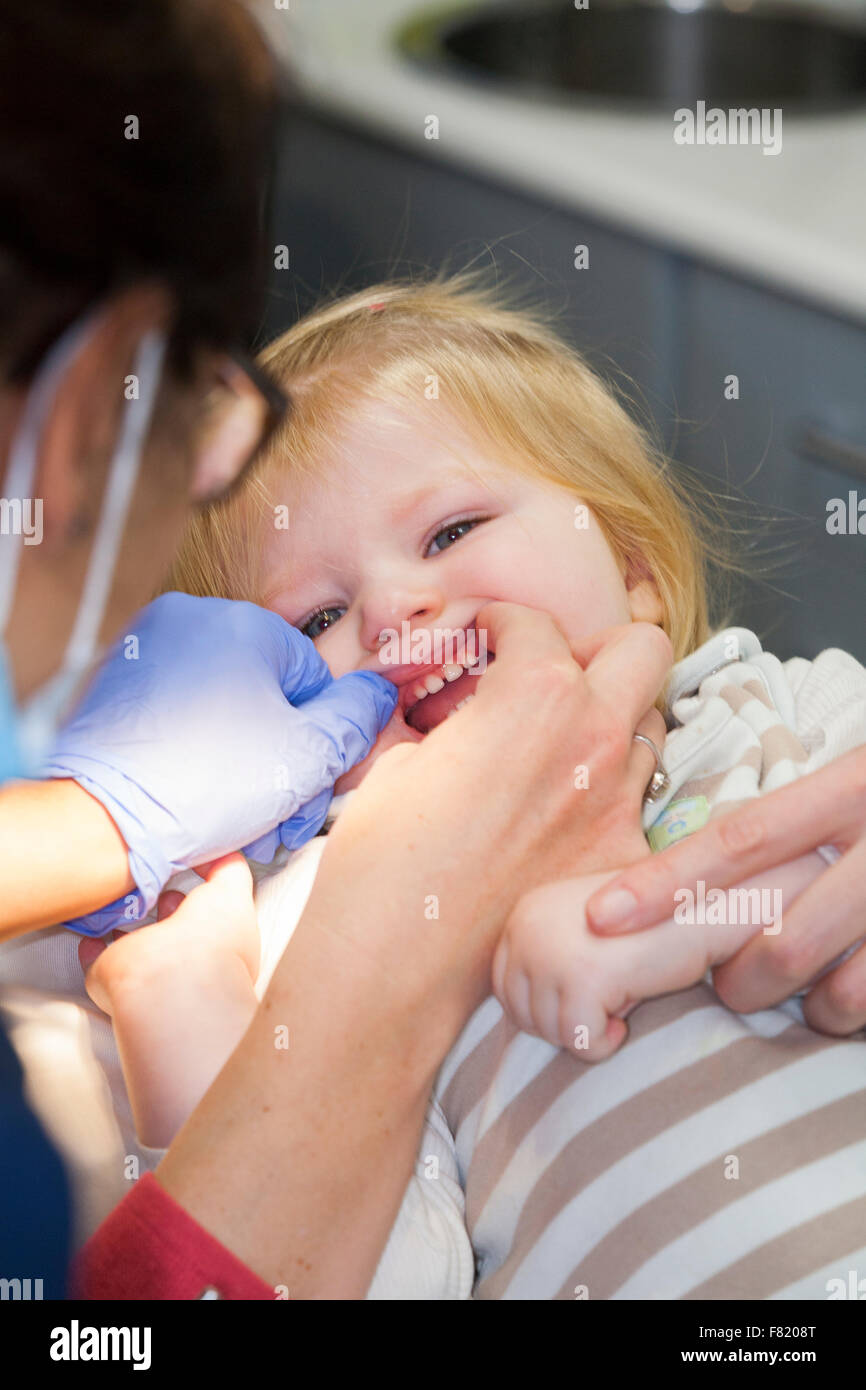 Baby toddler girl 1 anno di un anno di età bambino durante il suo primo primo check up con il dentista per bambini / bambini pratica dentale. Regno Unito Foto Stock