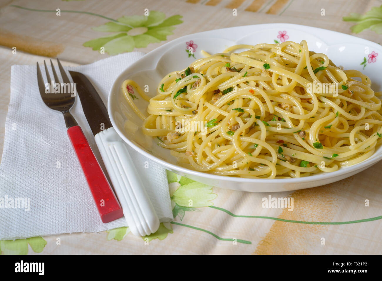 Un piatto di spaghetti con le vongole (pasta e rivendicazioni) una forcella rossa e un coltello bianco, tipico di pesce italiano Foto Stock