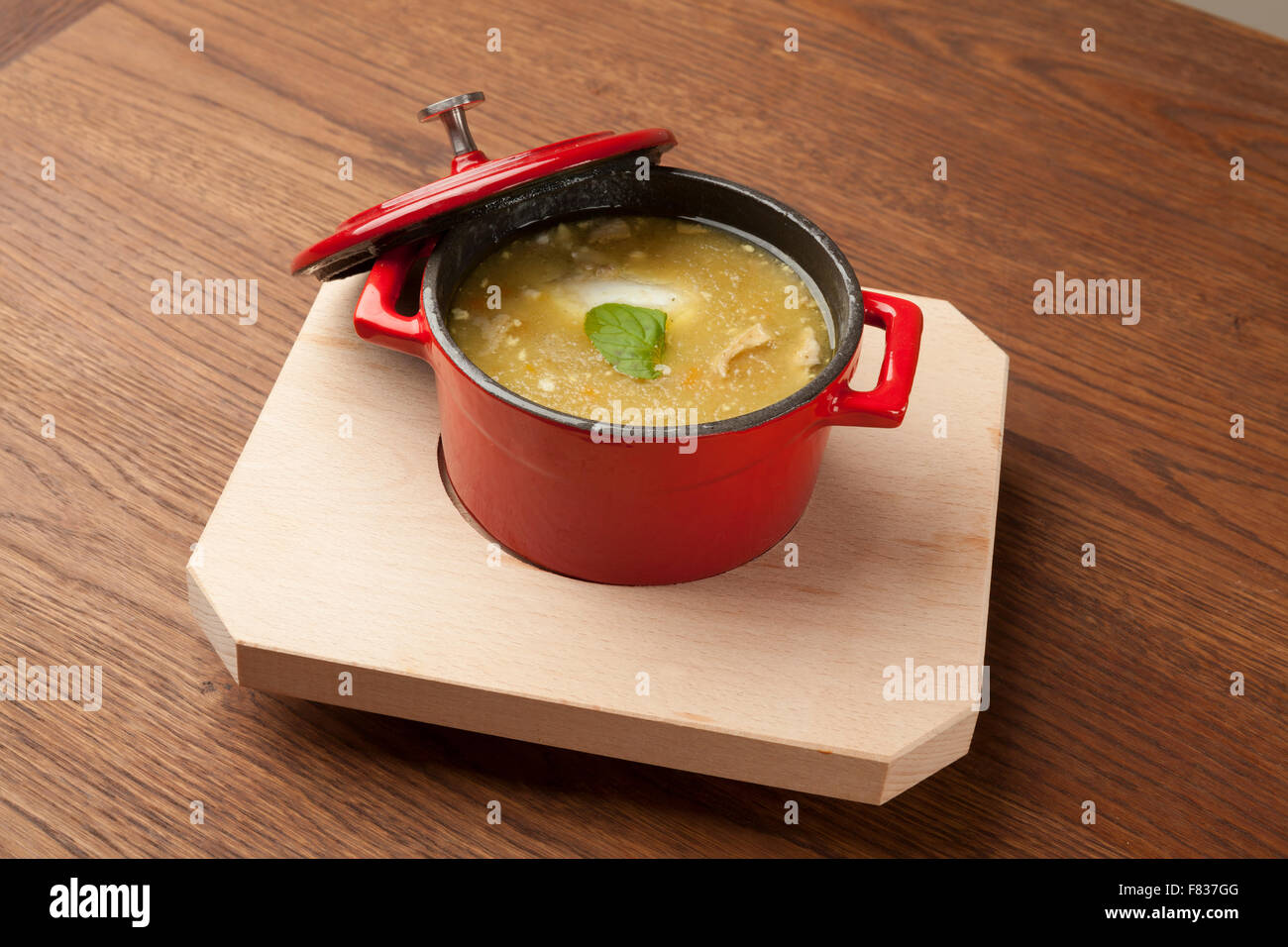 Zuppa di pollo in una ciotola rossa sul piatto di legno Foto Stock
