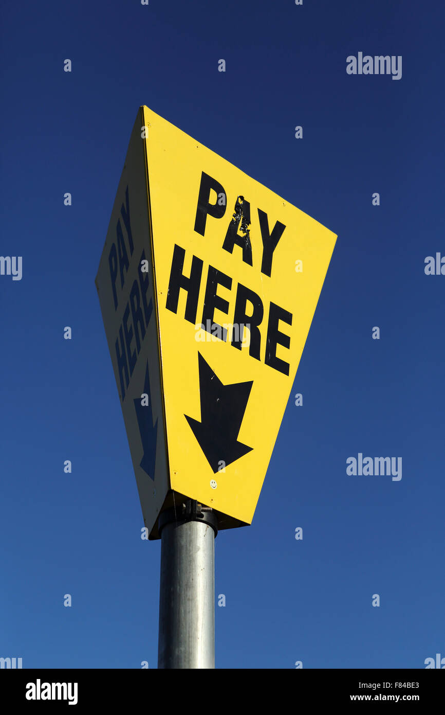 Un segno punti persone "Pagare qui' in corrispondenza di un parcheggio auto di Lewes, Inghilterra. Il cartello giallo è contrastata contro il cielo blu. Foto Stock