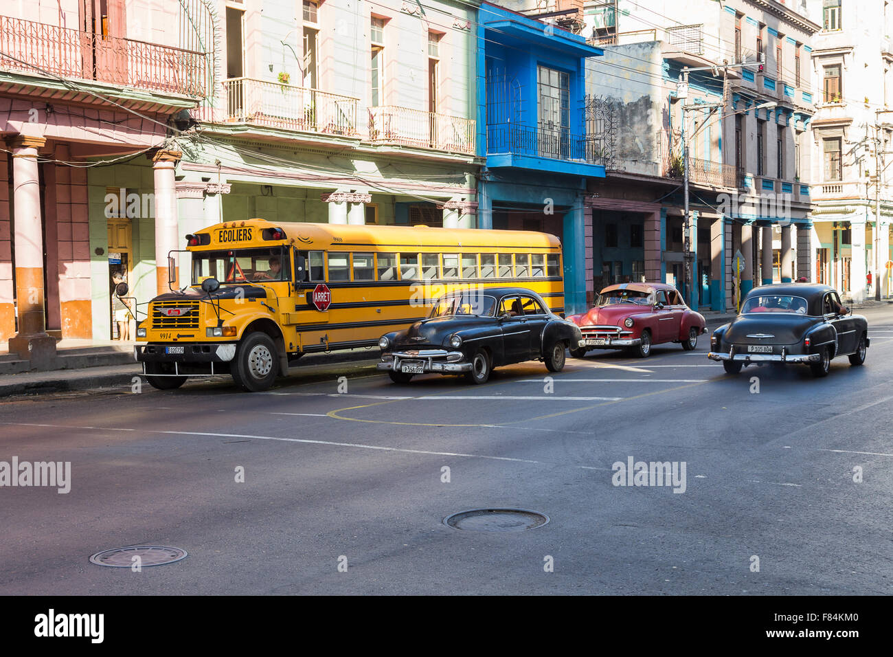 La dimensione del giallo scuolabus può essere visto qui contro alcune vecchie auto nel centro di Havana. Foto Stock