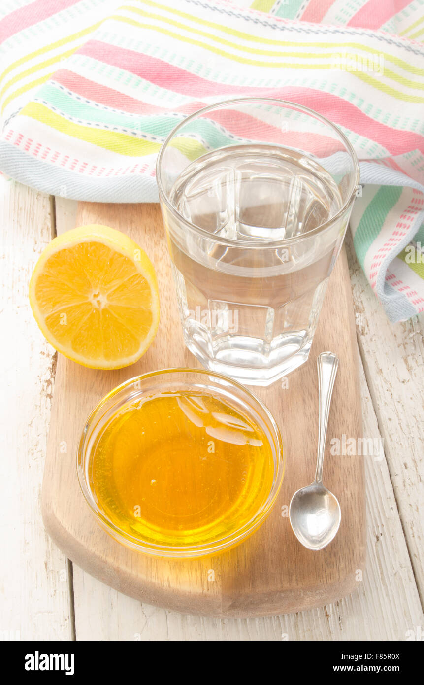 Acqua calda in un bicchiere sulla tavola di legno con il limone, il miele e il cucchiaio Foto Stock