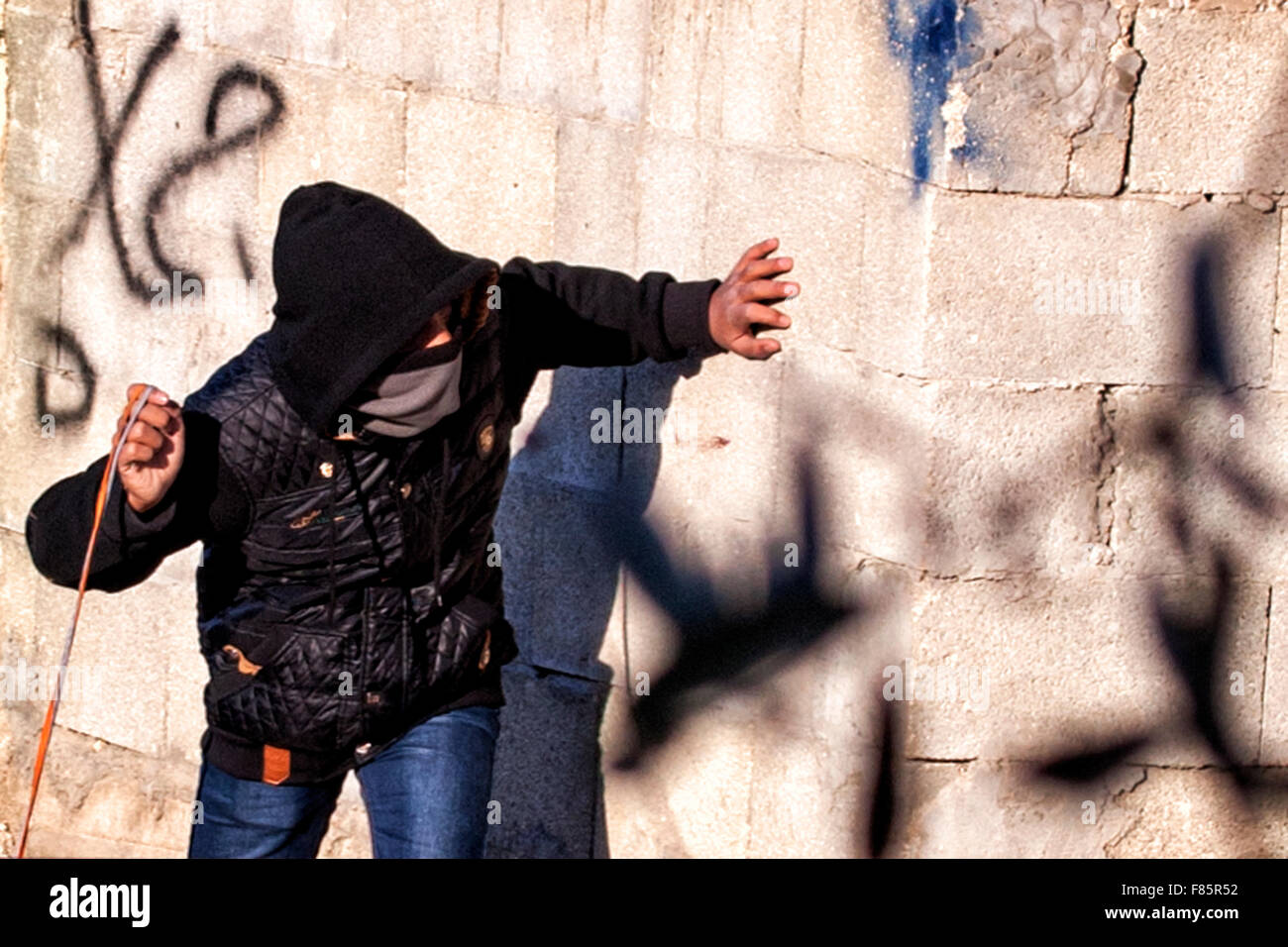 Un palestinese prepara il suo slingshot dietro il rivestimento di una parete durante gli scontri con le forze israeliane vicino a Ramallah in Cisgiordania Foto Stock
