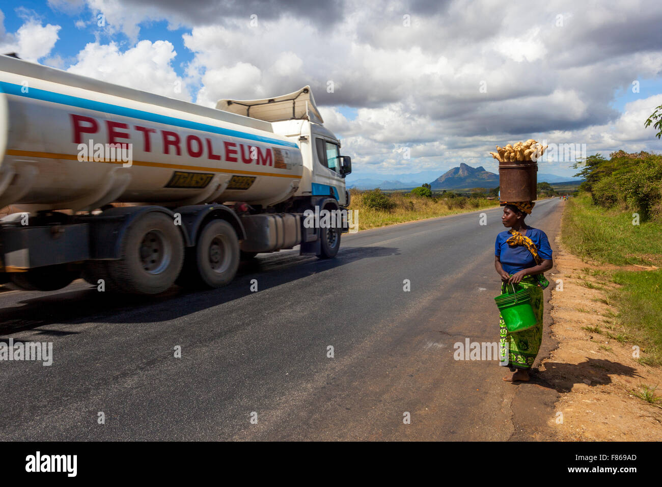Una povera donna della Tanzania portando la sua misera produrre per il mercato locale quando il passaggio di un camion a benzina incarna il divario in termini di ricchezza. Foto Stock