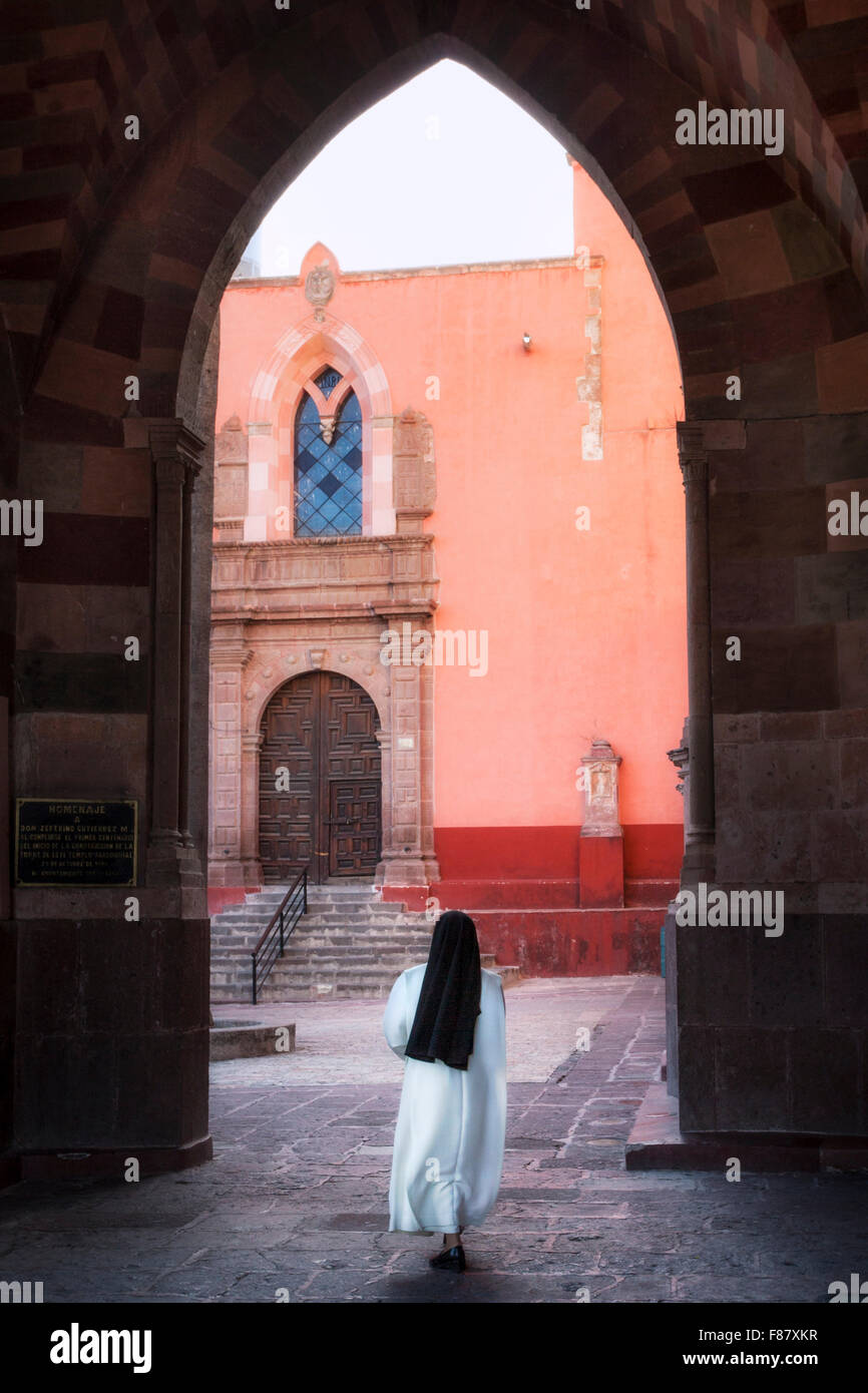 Una suora lascia la Basilica attraverso un ingresso arcuato in San Miguel De Allende, Messico. Foto Stock