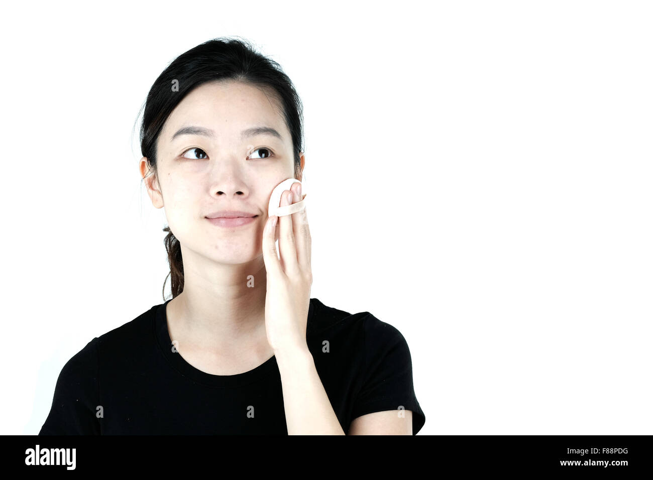 Carino ragazza asiatica mettere sulla fondazione polvere sul viso, isolati su sfondo bianco Foto Stock