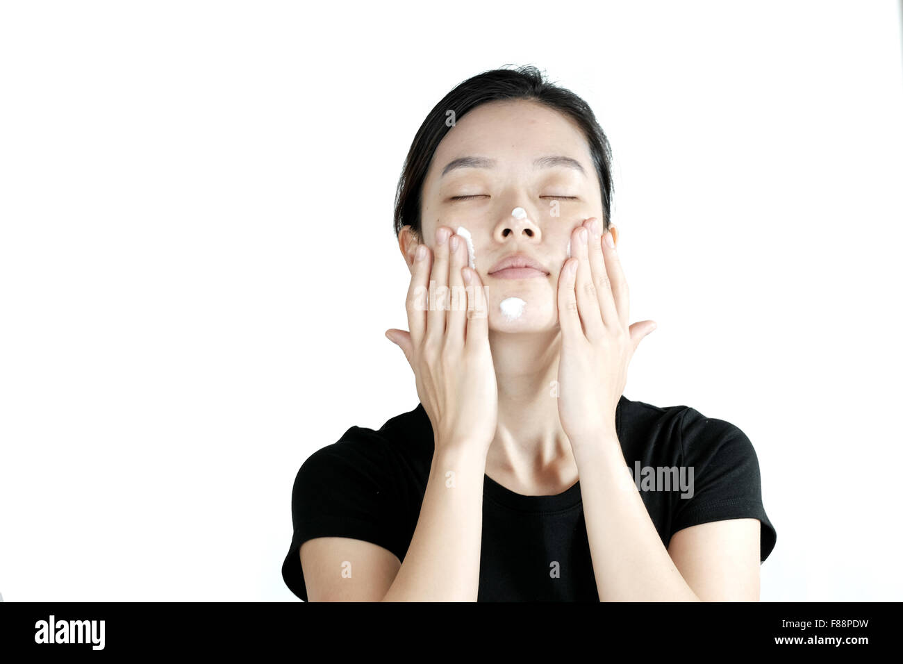 Carino ragazza asiatica di applicare la crema lozione sulla faccia, isolati su sfondo bianco Foto Stock