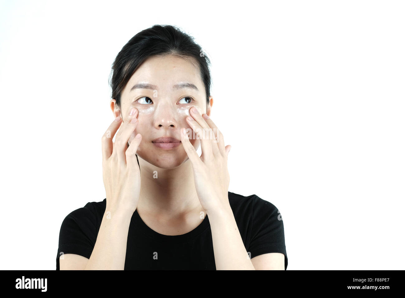 Carino ragazza asiatica di applicare la crema lozione sulla faccia, isolati su sfondo bianco Foto Stock
