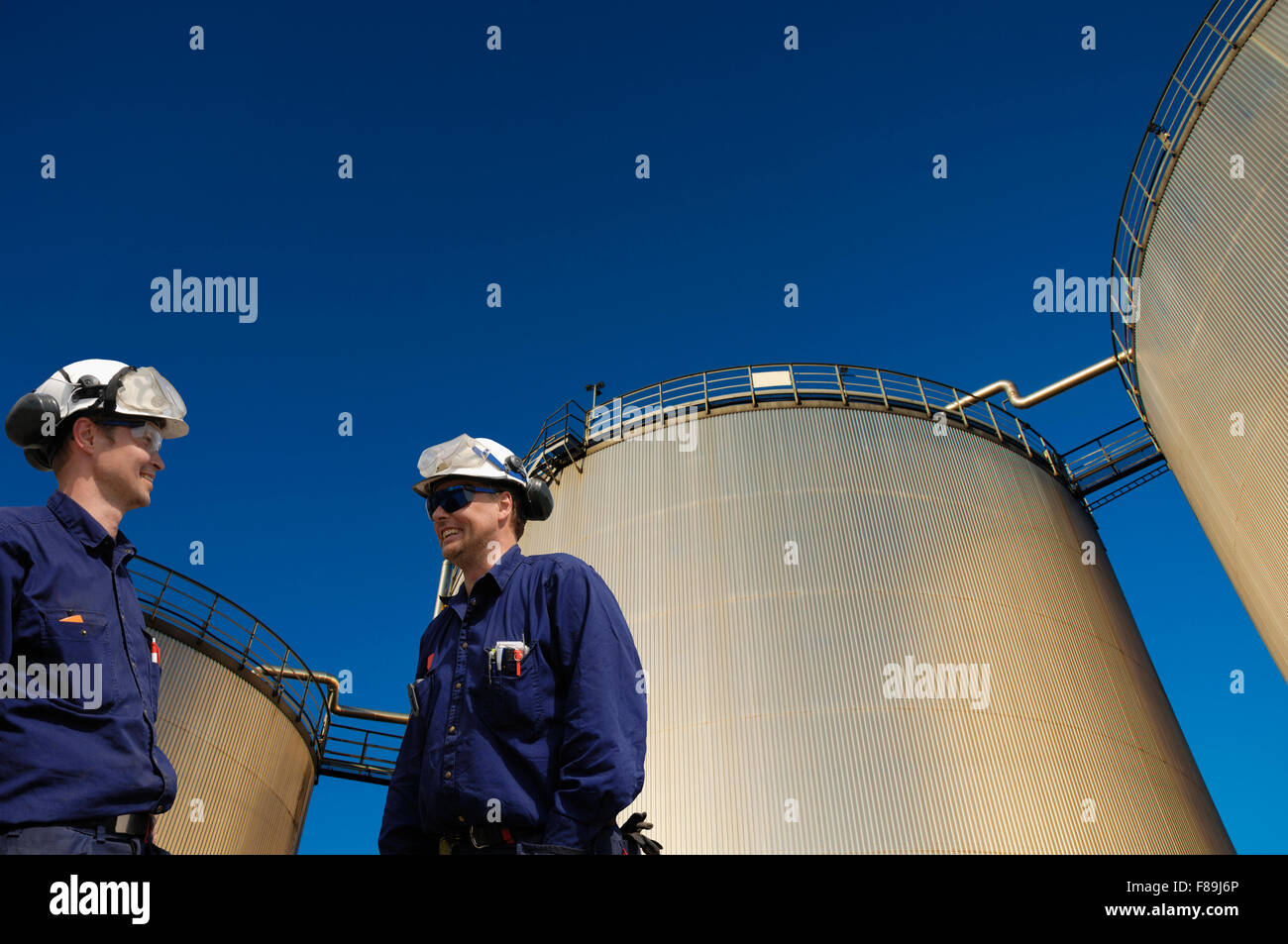 Due olio-lavoratori in hardhat con combustibile grande-serbatoi in background Foto Stock