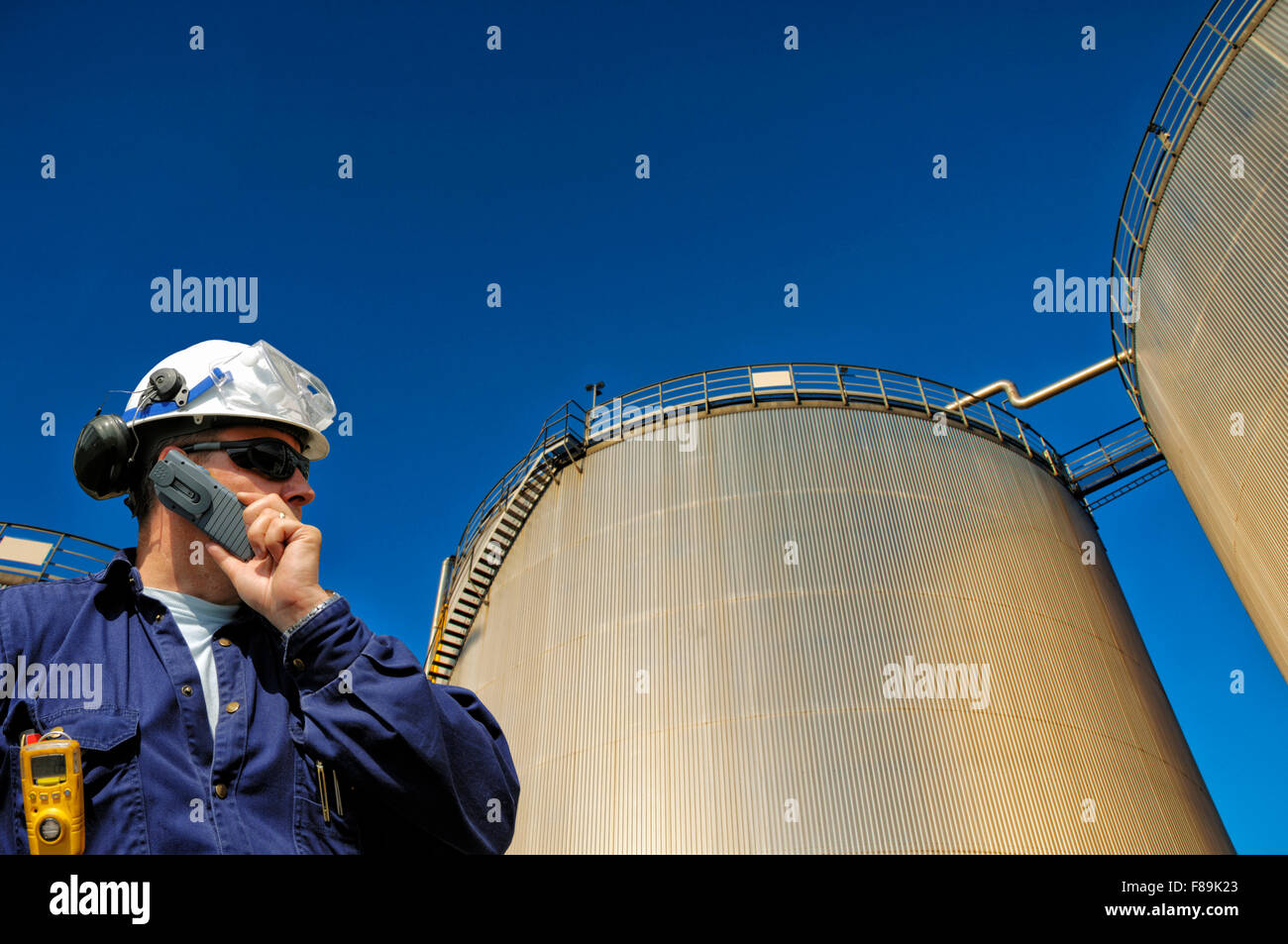 Lavoratore di olio e giganteschi serbatoi di carburante e torri, raffineria chimica Foto Stock