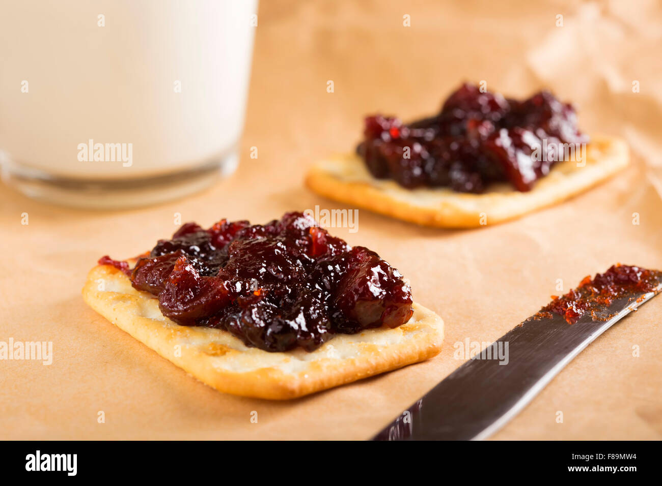 Confettura di mele cotogne su saltine crackers con un bicchiere di latte sulla carta Foto Stock