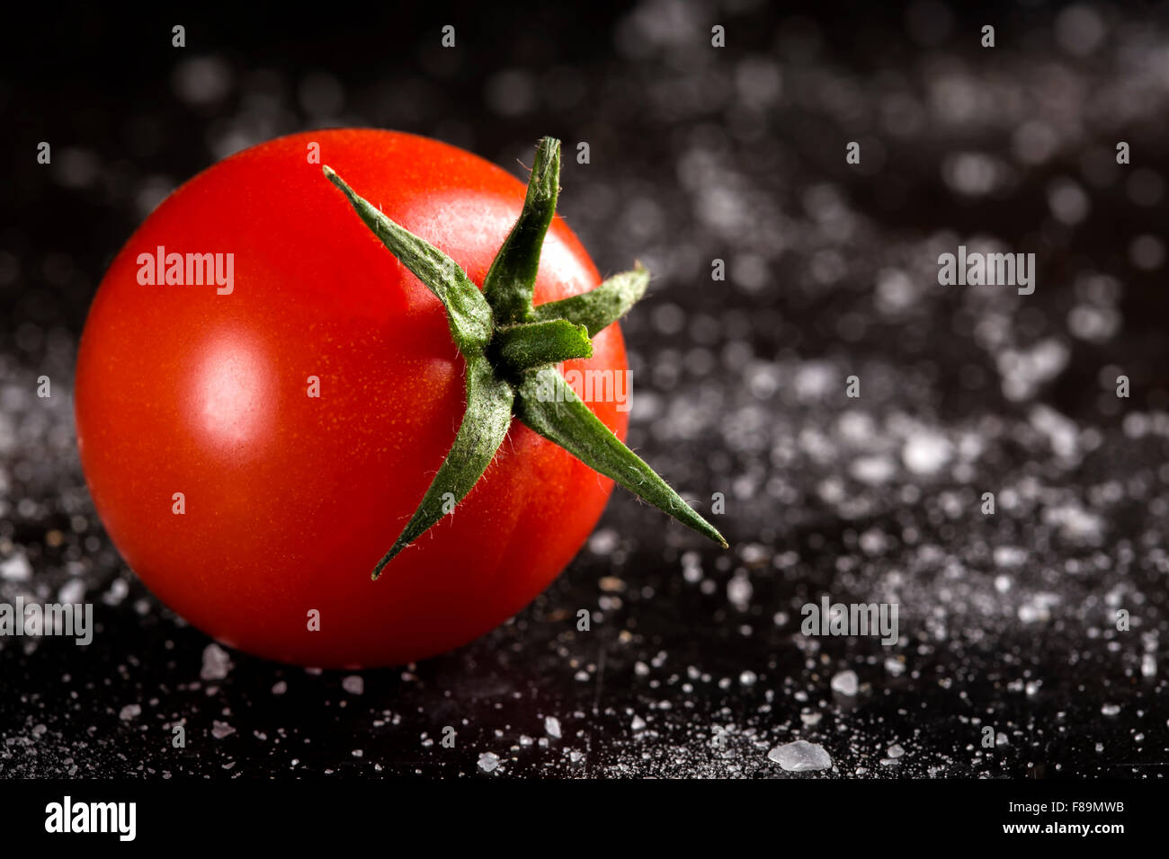 Un pomodoro ciliegino con sale su scuro dello sfondo metallico Foto Stock