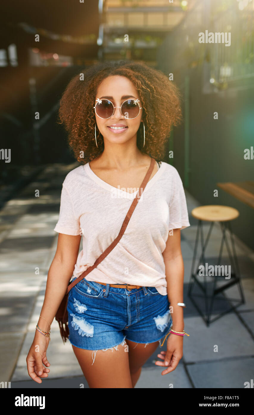Elegante donna africana indossando occhiali da sole in posa all'aperto.  Giovane e bella ragazza con i capelli ricci a casuals camminando sul  marciapiede Foto stock - Alamy
