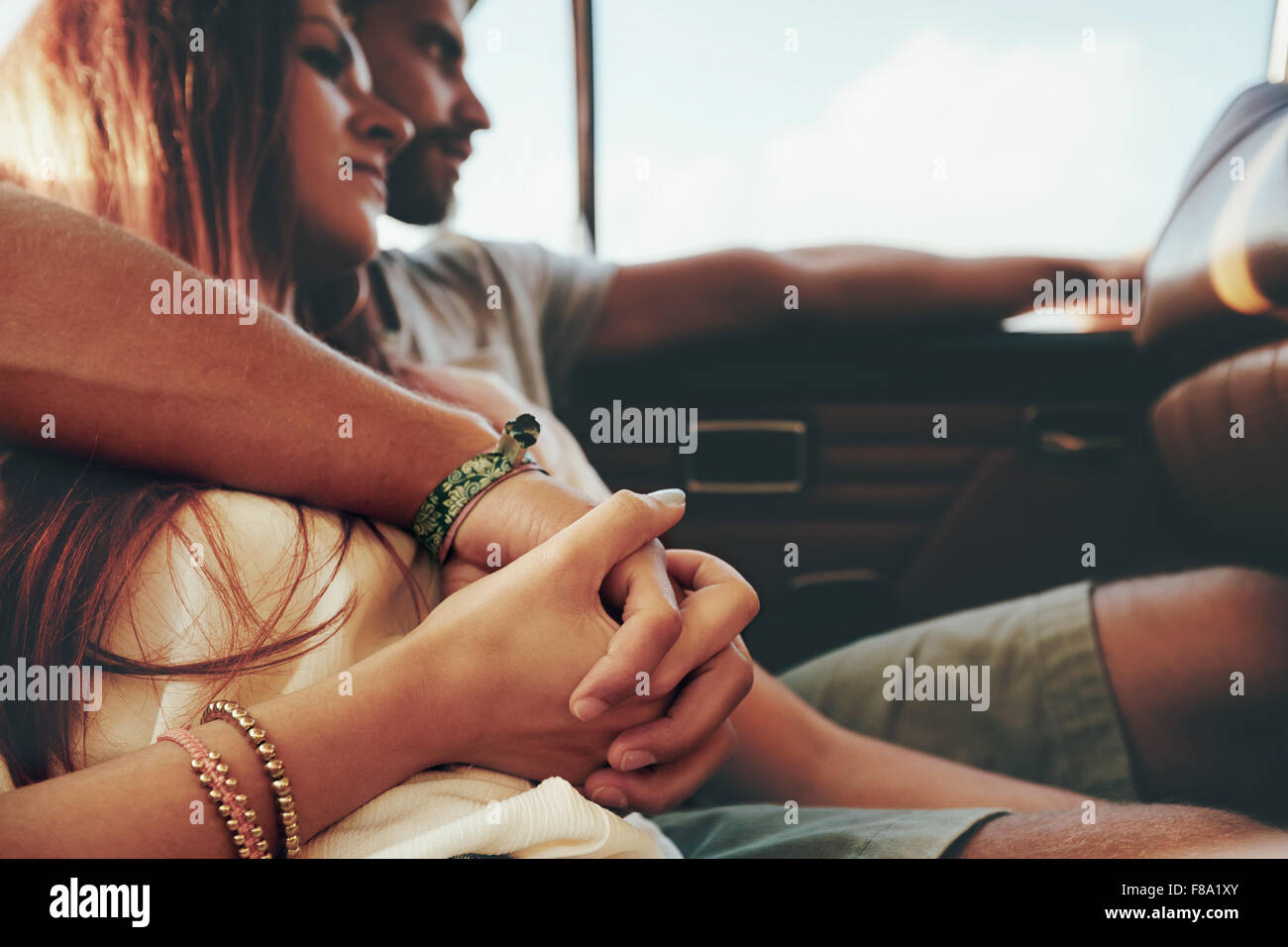 Affettuosa coppia giovane seduto nel sedile posteriore di una vettura andando sul viaggio. Focus sul giovane tenendo le mani. Foto Stock
