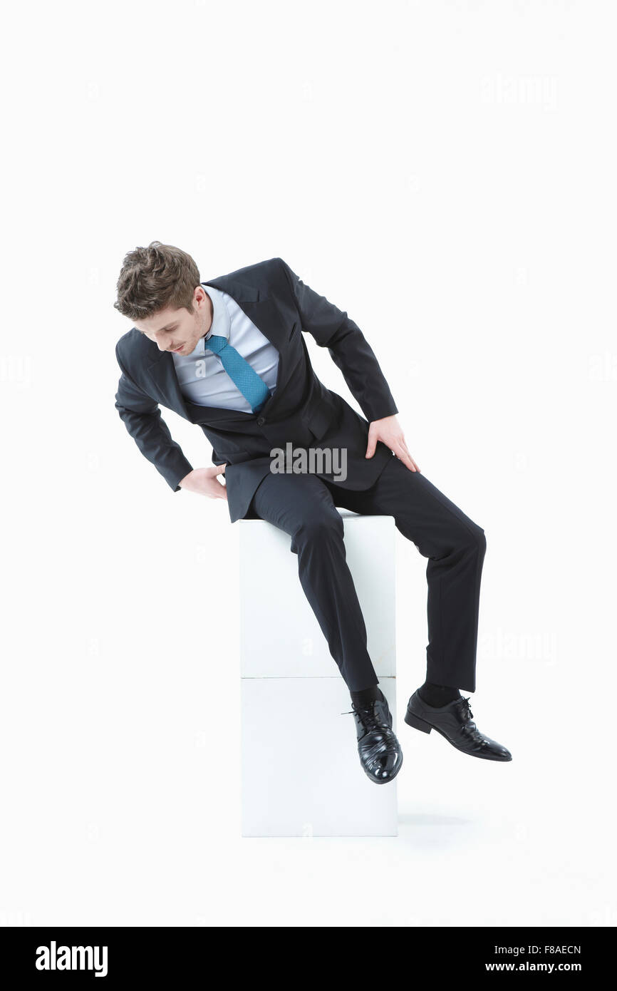 Uomo che guarda in basso mentre è seduto su due blocchi di colore bianco Foto Stock