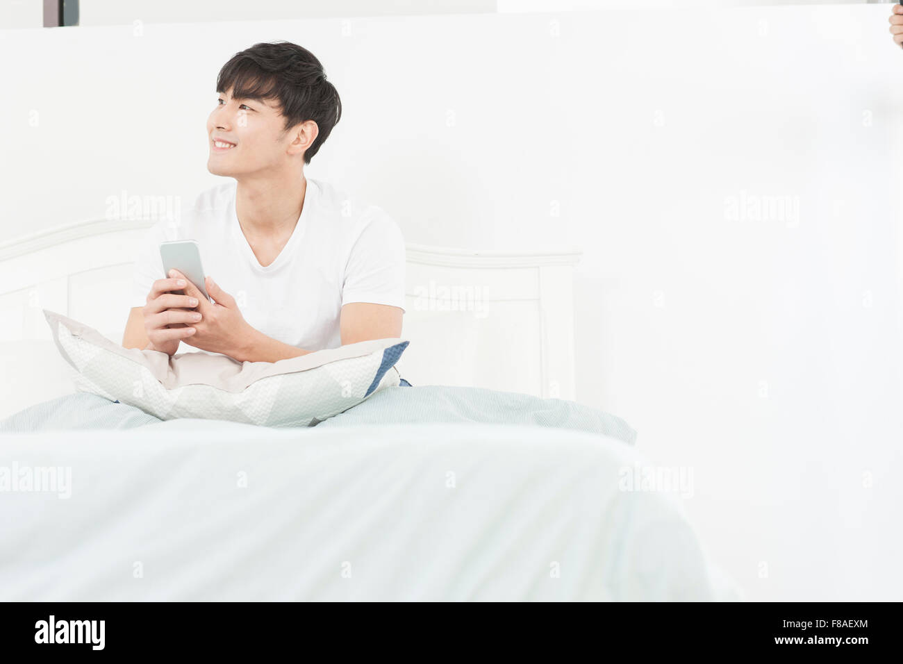 Uomo in possesso di un telefono cellulare e cercando sul lato sinistro nel letto Foto Stock