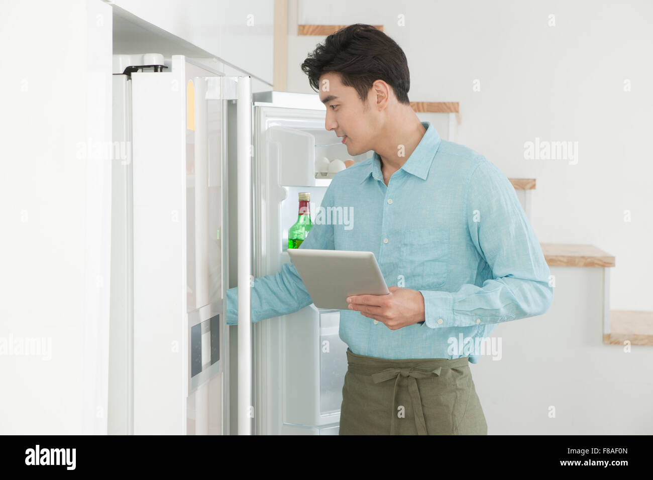 Uomo che guarda all'interno del frigo con il mantenimento di un tablet PC Foto Stock