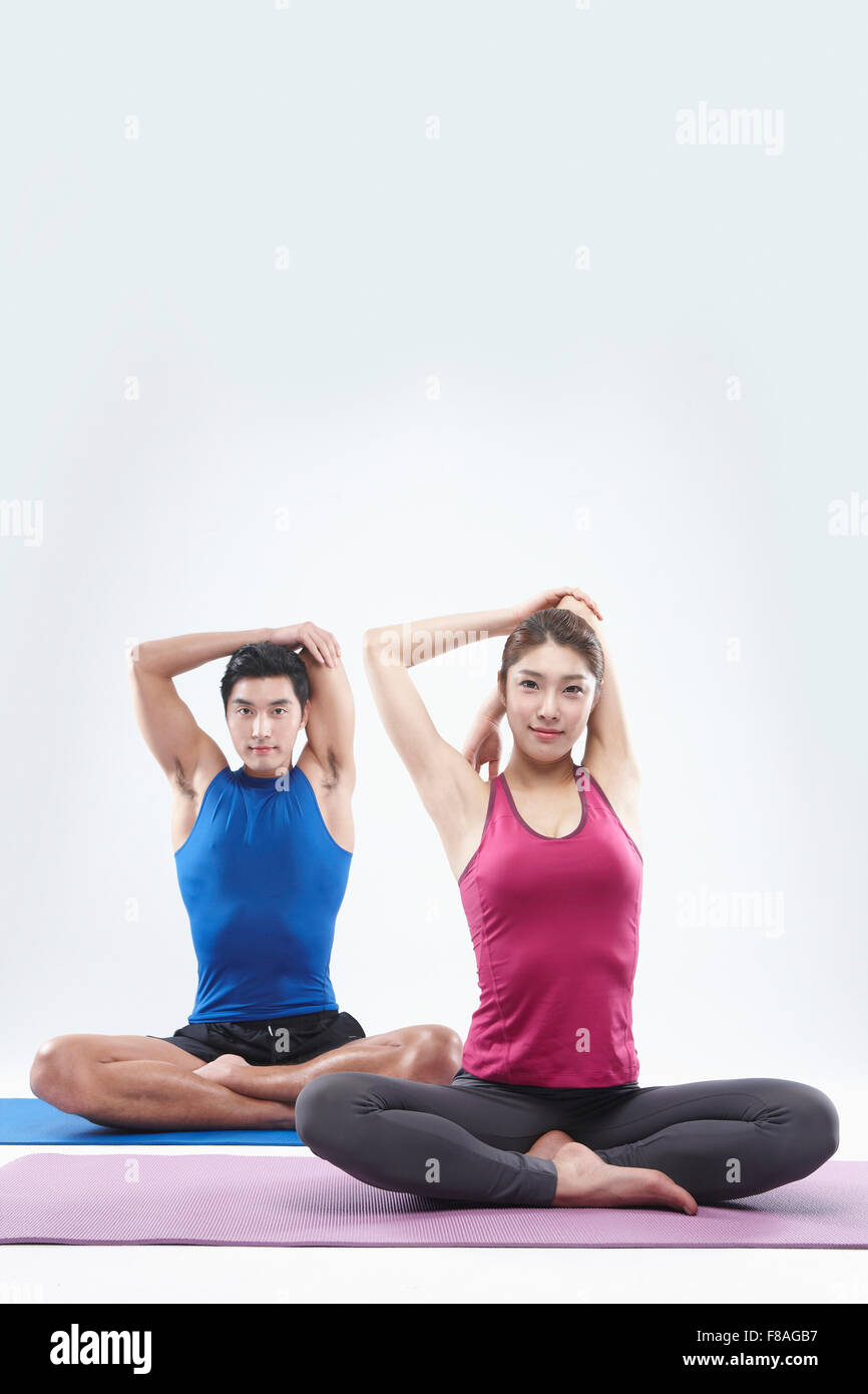 Un giovane seduto sul materassino yoga e allungando le braccia indietro verso il basso Foto Stock