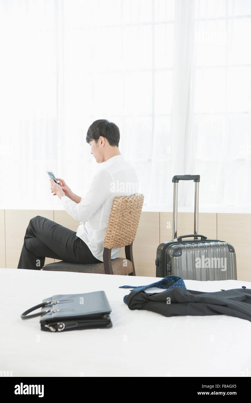 Torna l'aspetto di un uomo seduto sulla sedia guardando al suo tablet PC dietro il letto con altri business-oggetti correlati Foto Stock