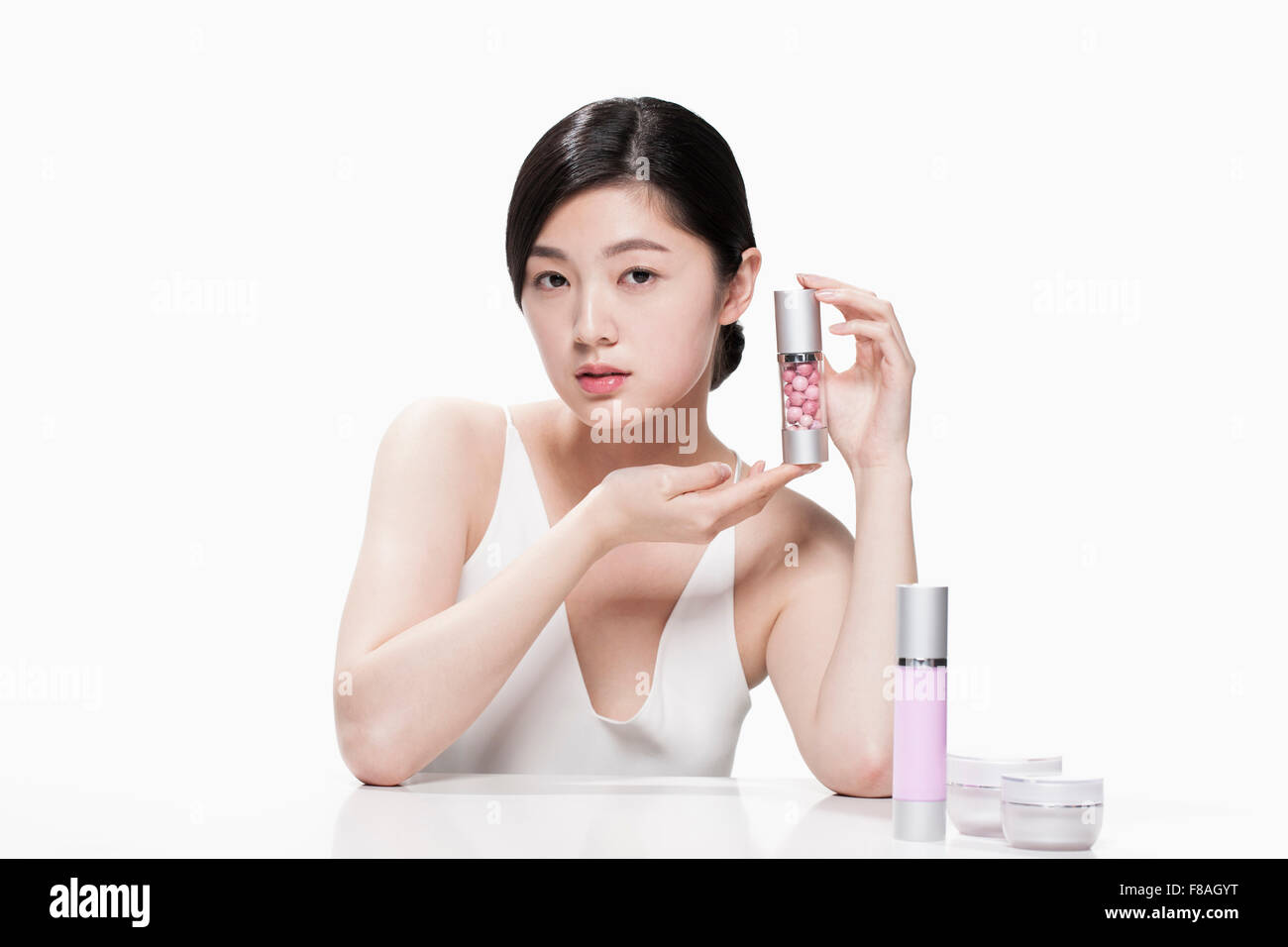 Giovane donna asiatica tenendo un contenitore per cosmetici con due mani e appoggio le sue braccia sul tavolo Foto Stock