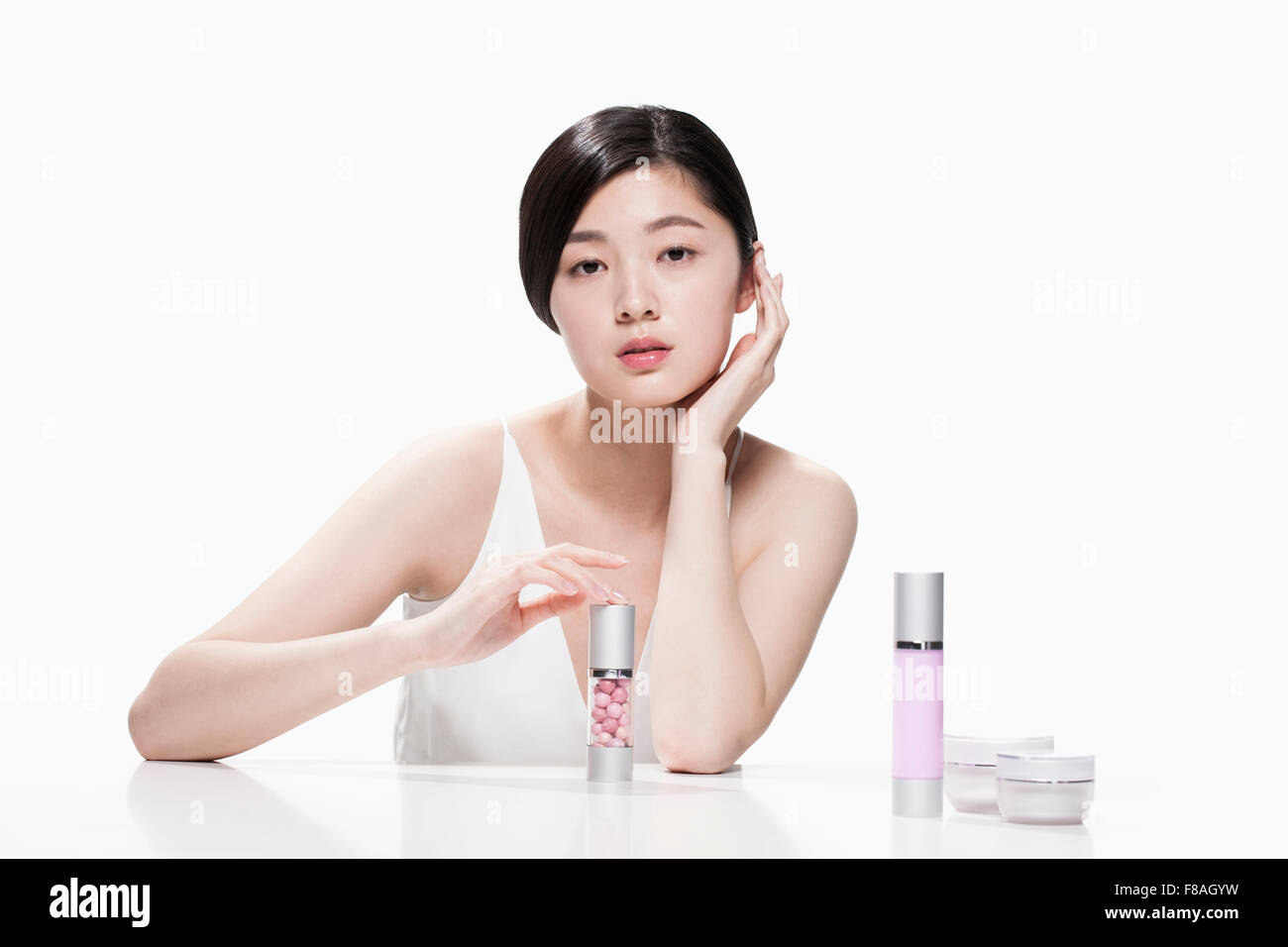 Giovane donna asiatica toccando un contenitore cosmetico sulla tavola con l'altra mano sotto il suo mento Foto Stock