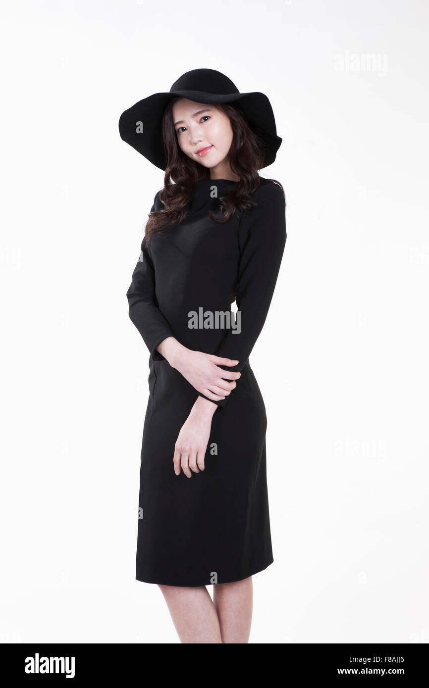 Giovane donna in black hat e abito nero facendo una posa con le sue mani verso il basso Foto Stock