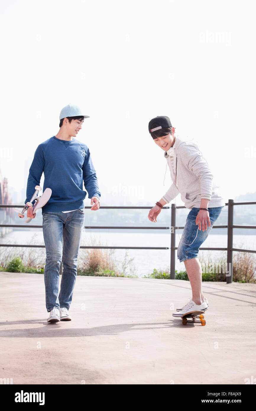 Giovane uomo in un cappuccio nero lo skateboard e l'altro uomo in un tappo blu tenendo la sua skateboard sotto il suo braccio Foto Stock