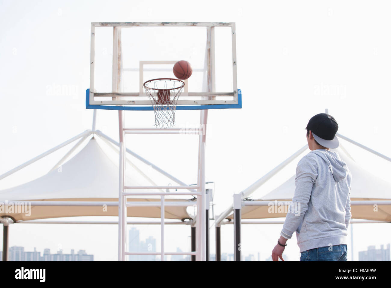 Giovane uomo in un cappuccio di gettare una palla al campo di pallacanestro Foto Stock