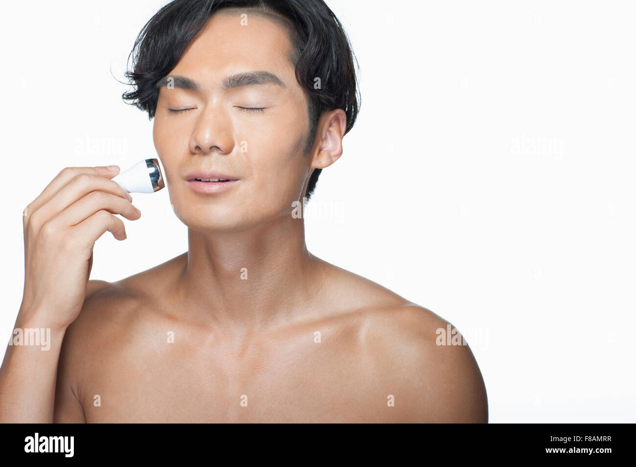 Ritratto di uomo asiatico usando una macchina per la cura della pelle con gli occhi chiusi Foto Stock