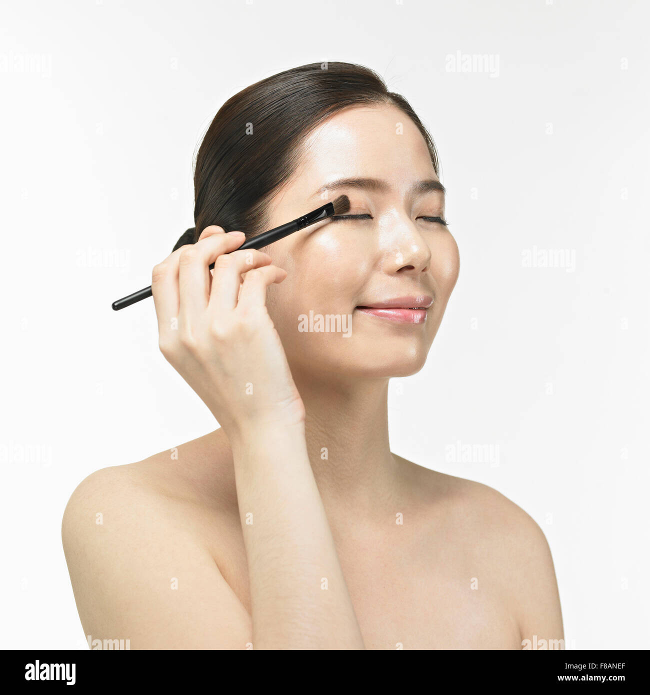 Ritratto di sorridente donna Coreana di chiudere gli occhi e applicazione di eye shadow con spazzola Foto Stock