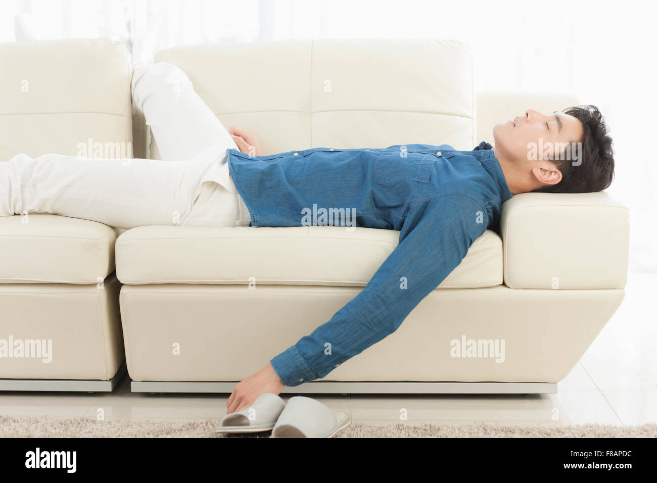 Vista laterale del giovane uomo sdraiato sul divano chiudendo gli occhi Foto Stock
