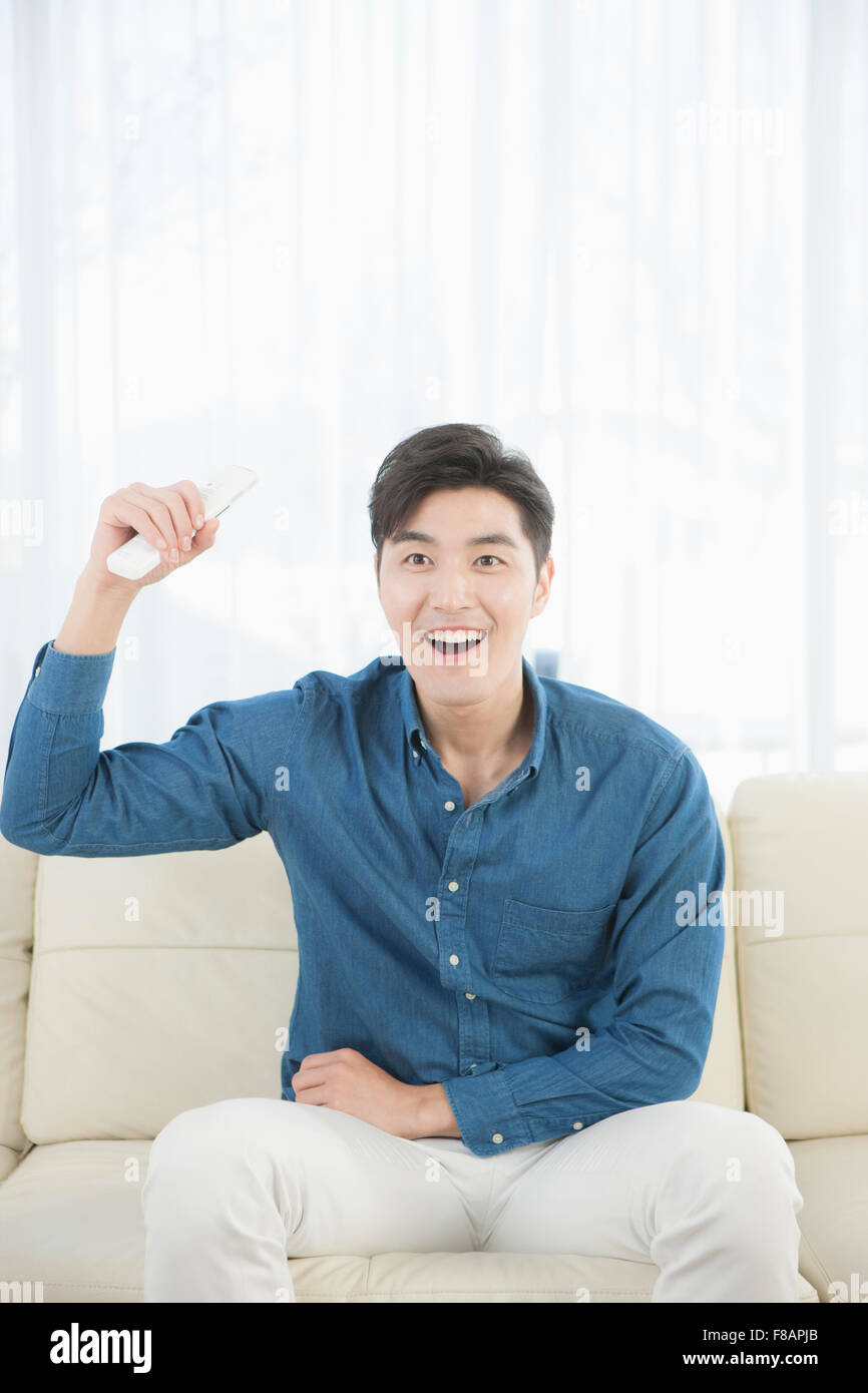 Sorridendo allegro giovane uomo in possesso di un telecomando seduto sul divano Foto Stock